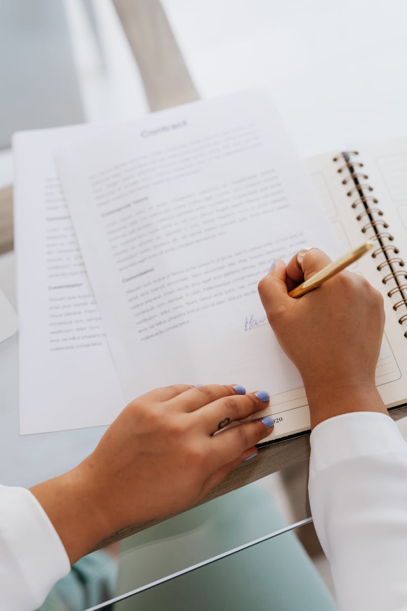 Woman signing a contract with a gold pen, focus on hands and document.